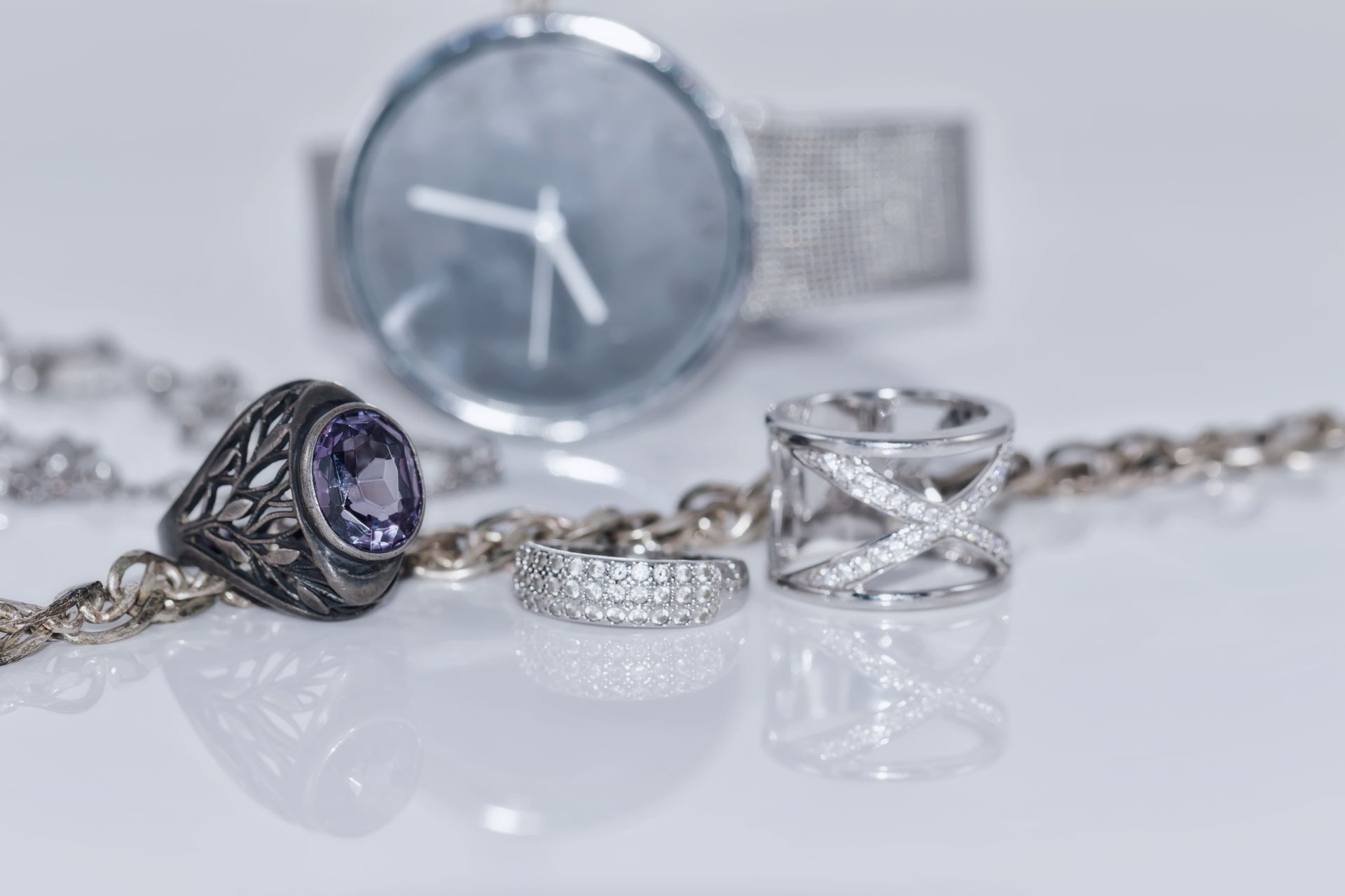 Primer plano de joyas de plata que incluyen anillos, collar y un reloj con fondo blanco.
