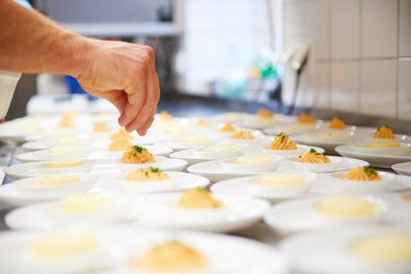 Das manuelle Anrichten kleiner Toppings auf Reihen weißer Dessertbecher in einer Küche oder einem Catering-Bereich