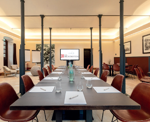 Langer Konferenztisch in einem hellen Besprechungsraum mit Stühlen und einer Präsentationswand am anderen Ende