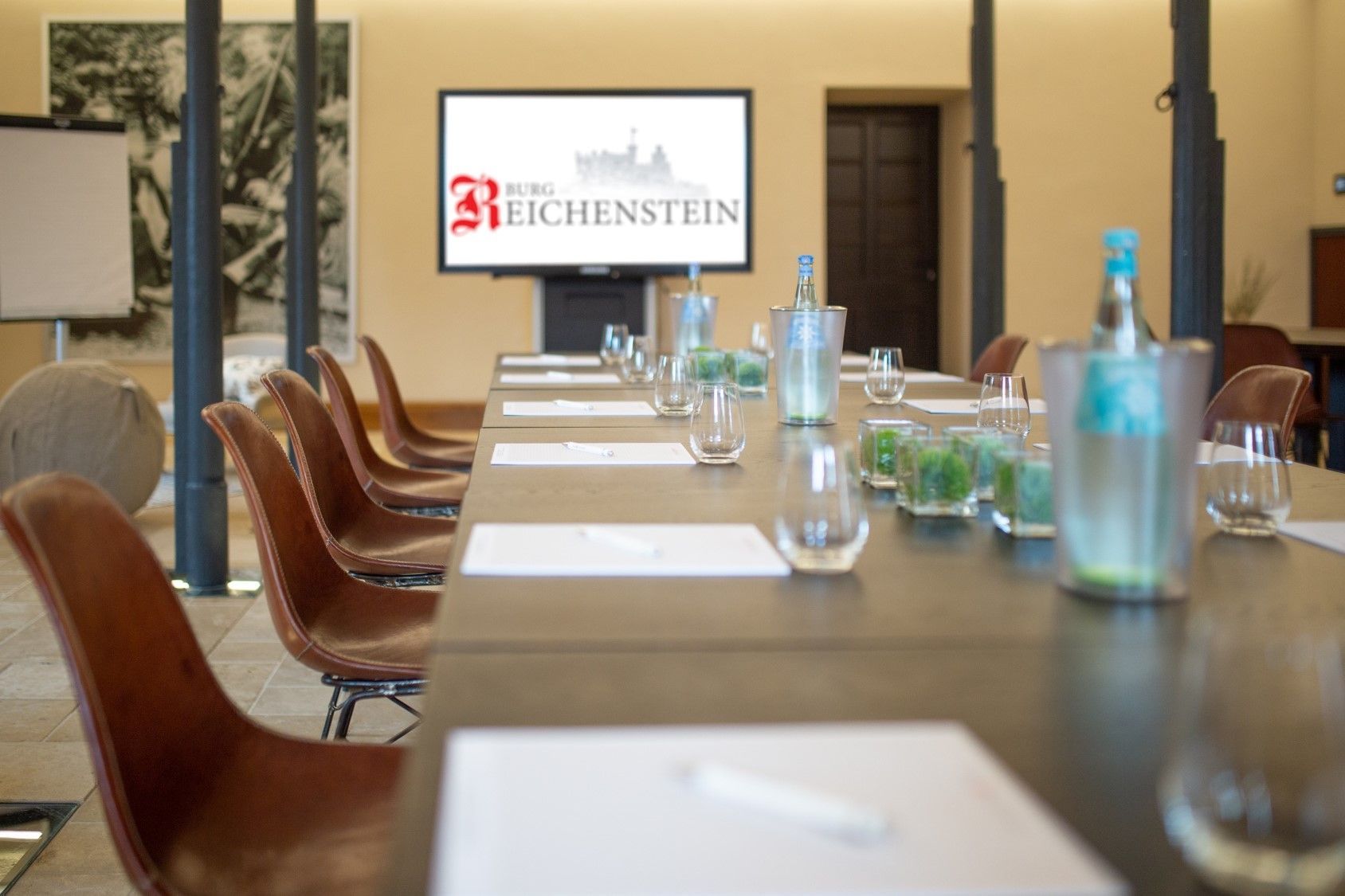 Konferenzraum mit einem langen Tisch, Wasserflaschen, Gläsern und einem Reichstein-Präsentationsbildschirm vorne.