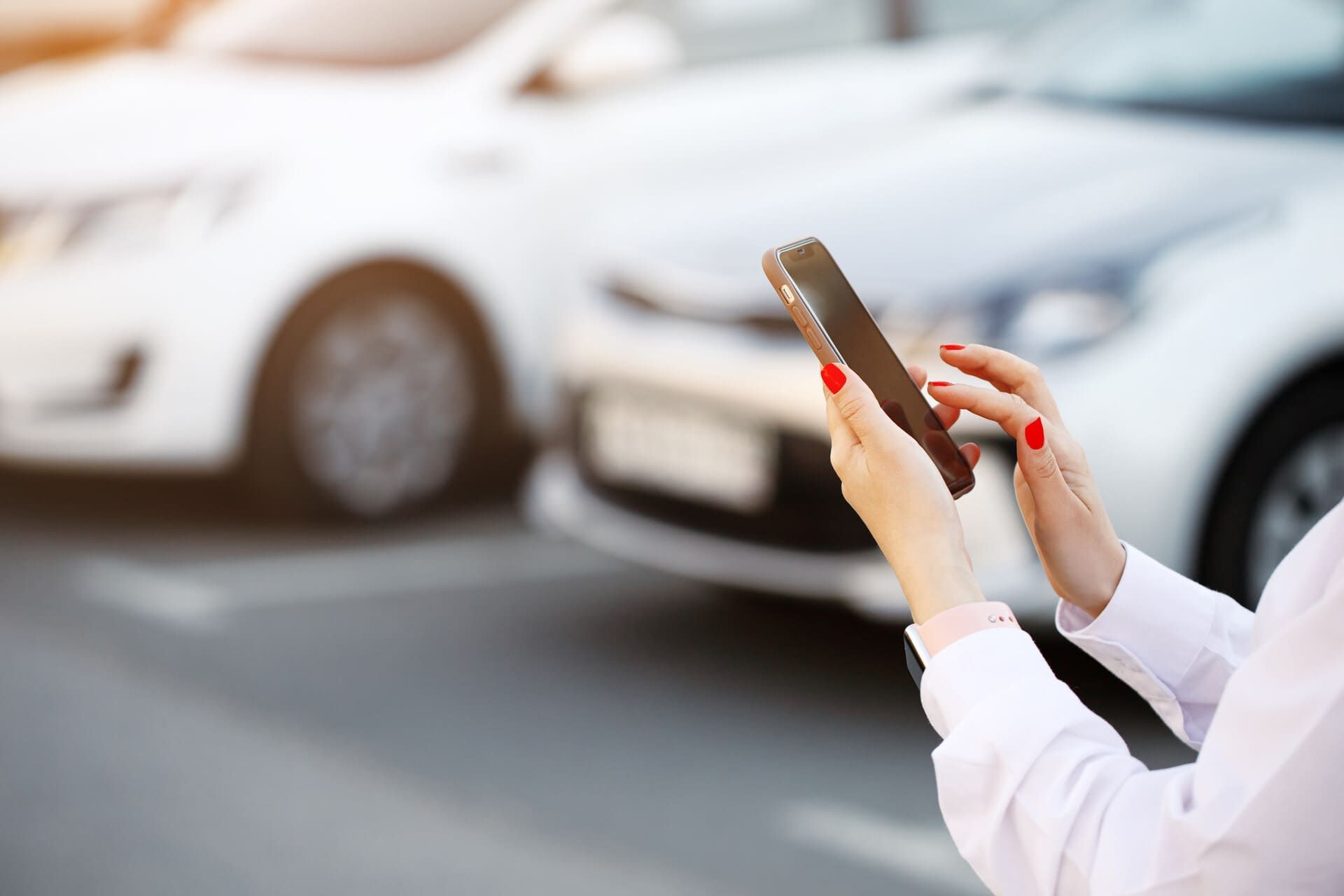 Mujer sosteniendo un teléfono frente a dos autos estacionados.