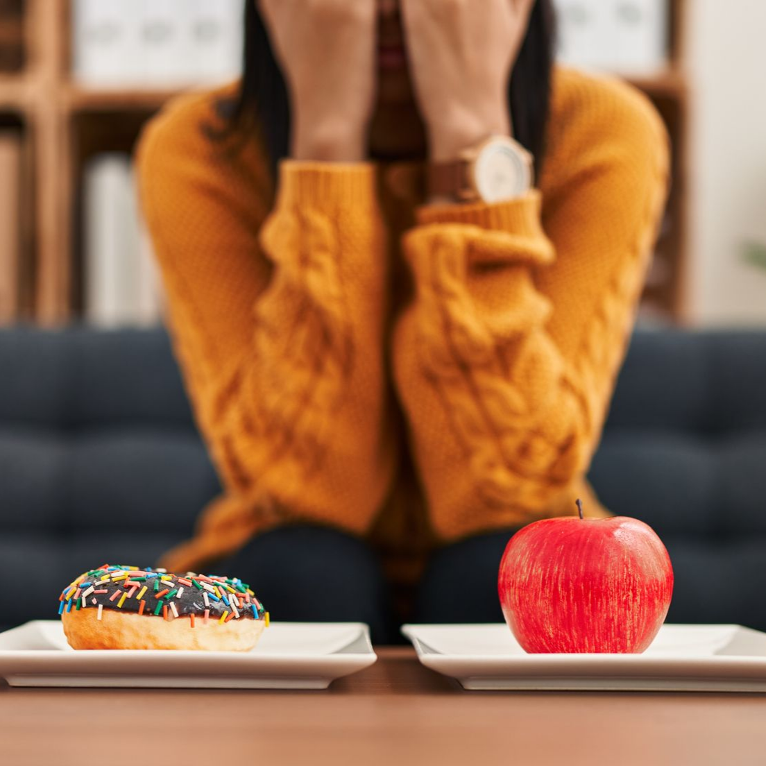 Personne les mains sur le visage, face à un beignet et une pomme sur des assiettes séparées.
