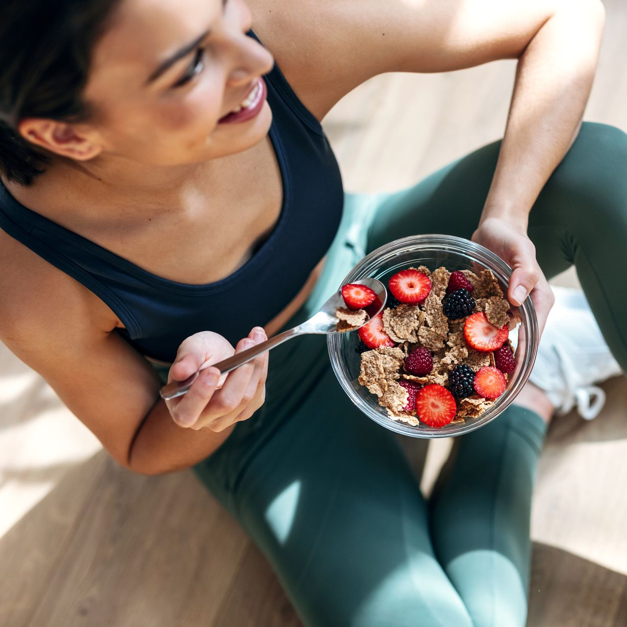 Une femme en tenue de sport mange des céréales avec des fruits.