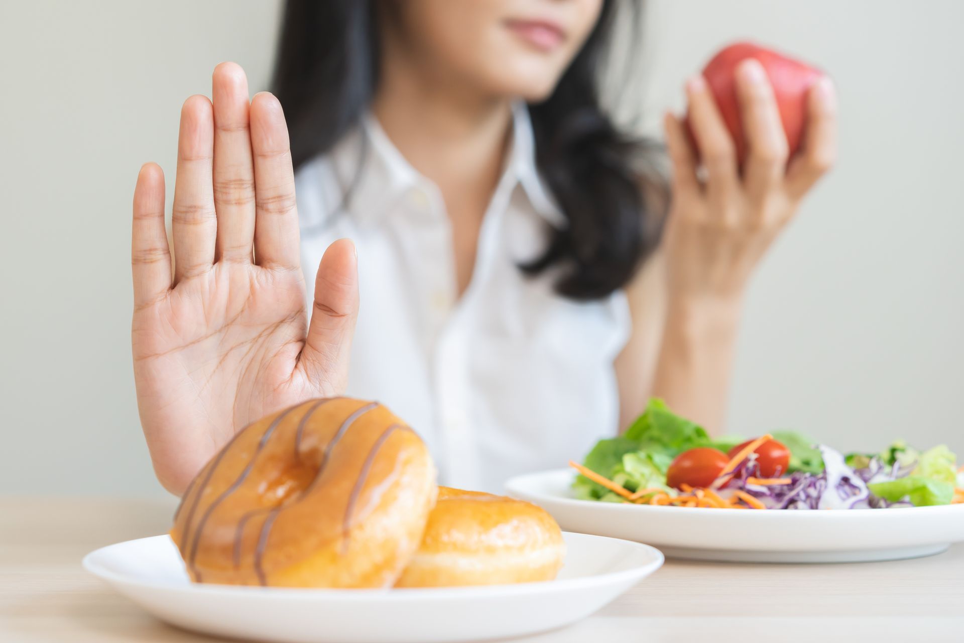 Une femme refuse des beignets, tenant une pomme, avec une salade à proximité.