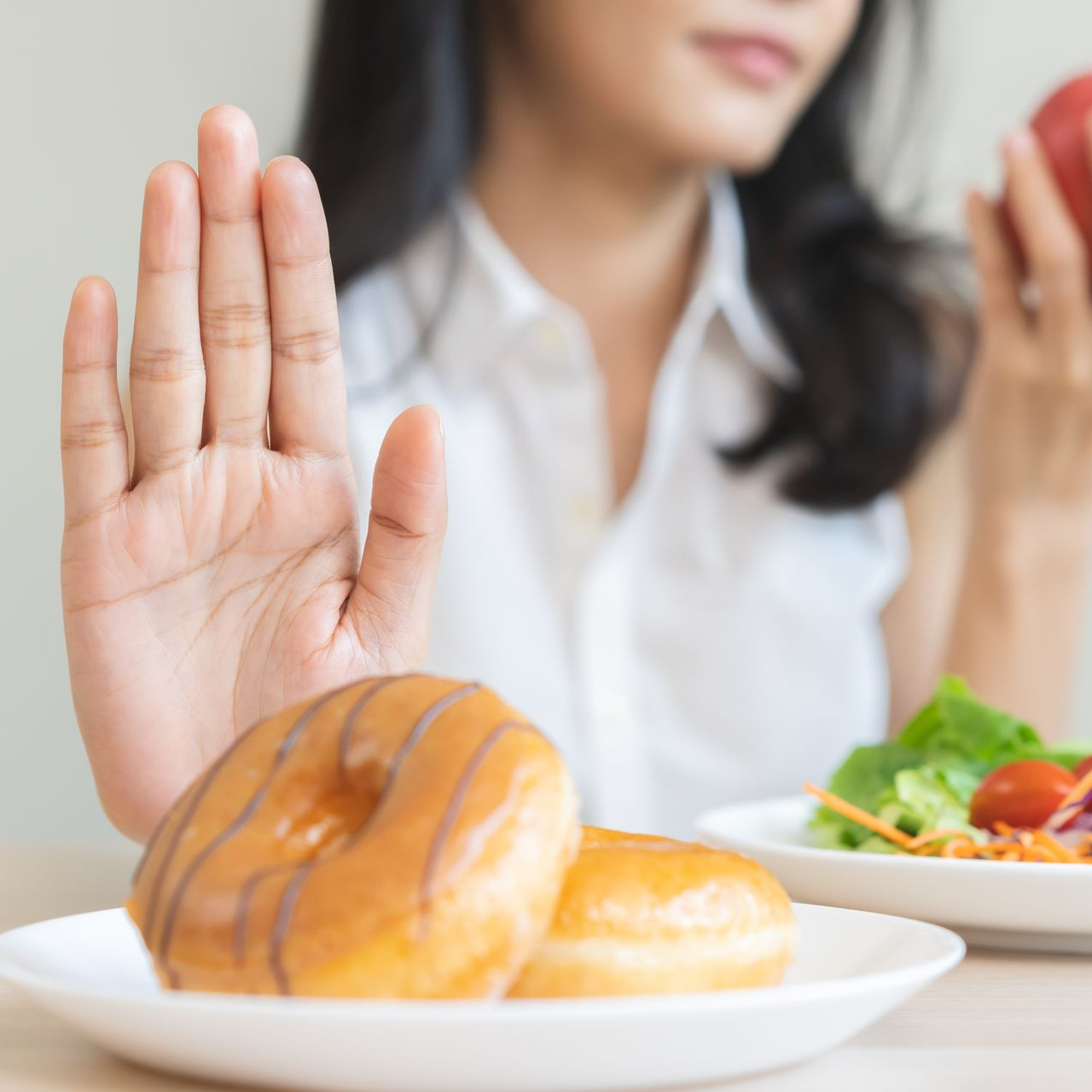Une femme refuse les beignets et se tourne vers une pomme et une salade.