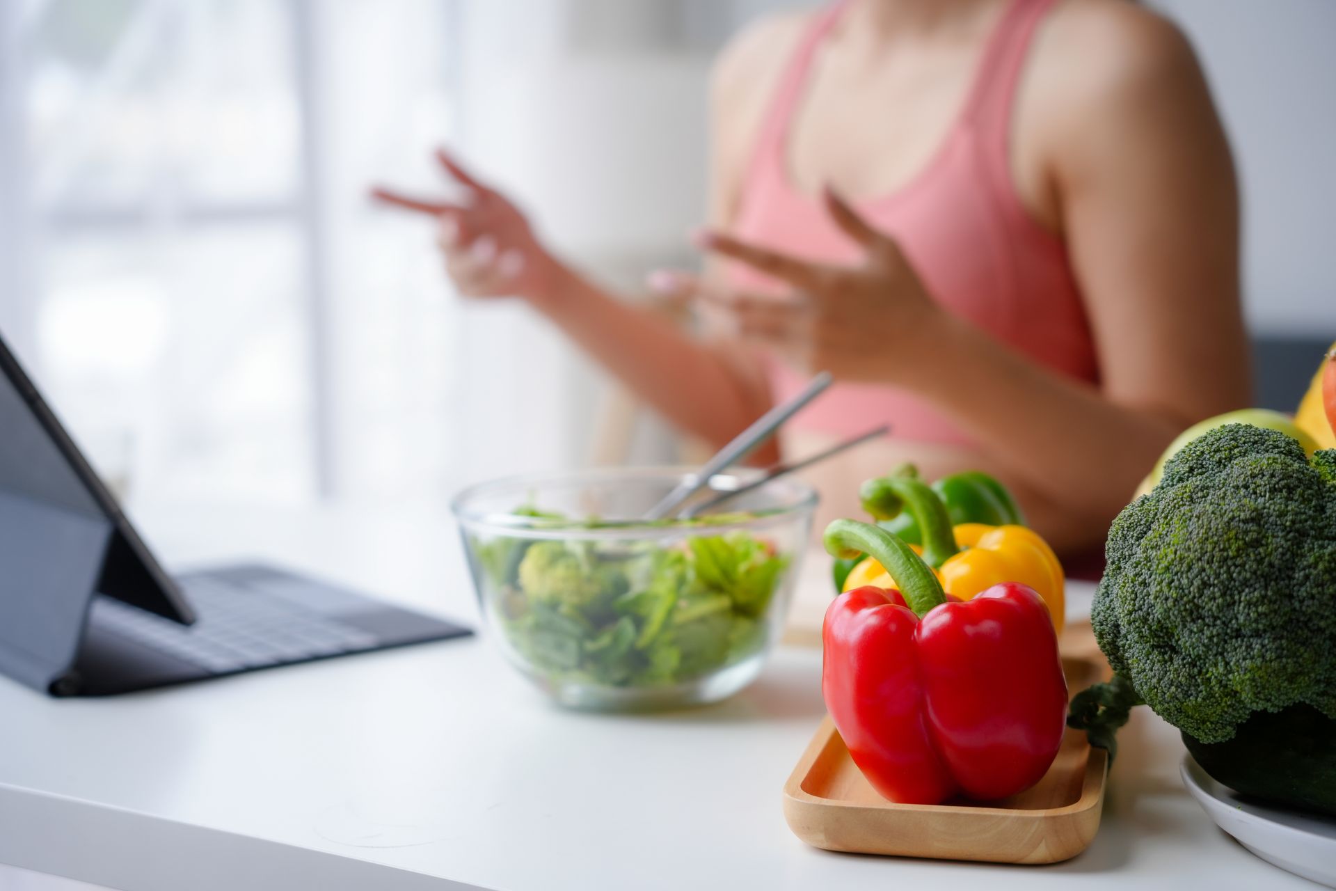 Une femme devant son ordinateur portable avec une salade et des légumes posés sur la table.