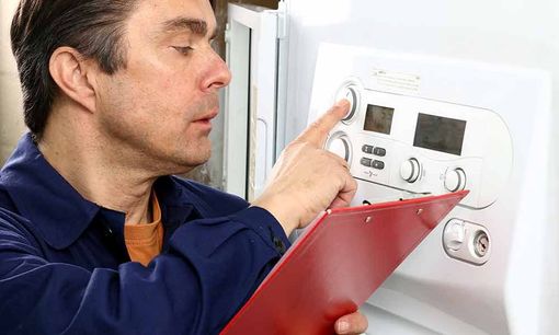 Ein Mann verstellt einen Wandthermostat, während er ein rotes Klemmbrett hält.
