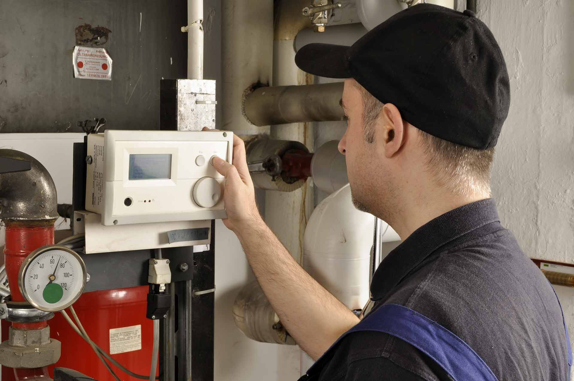 Ein Techniker justiert ein an der Wand montiertes Bedienfeld neben roten Rohrleitungen in einem Industrieraum.