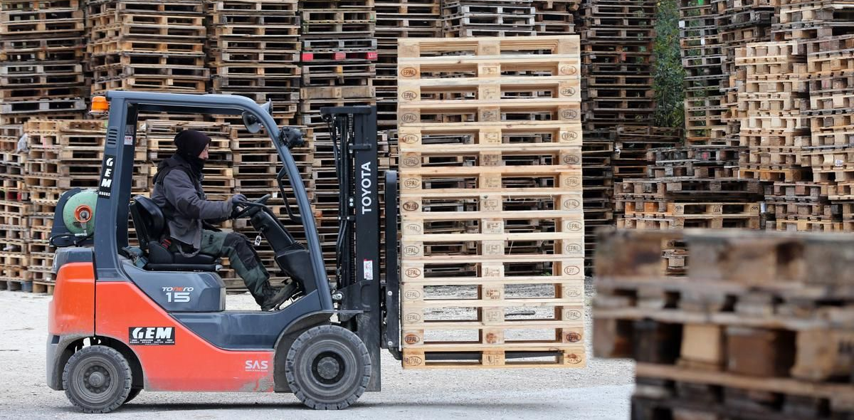 Un monsieur sur un élévateur porte un tas de palettes en bois