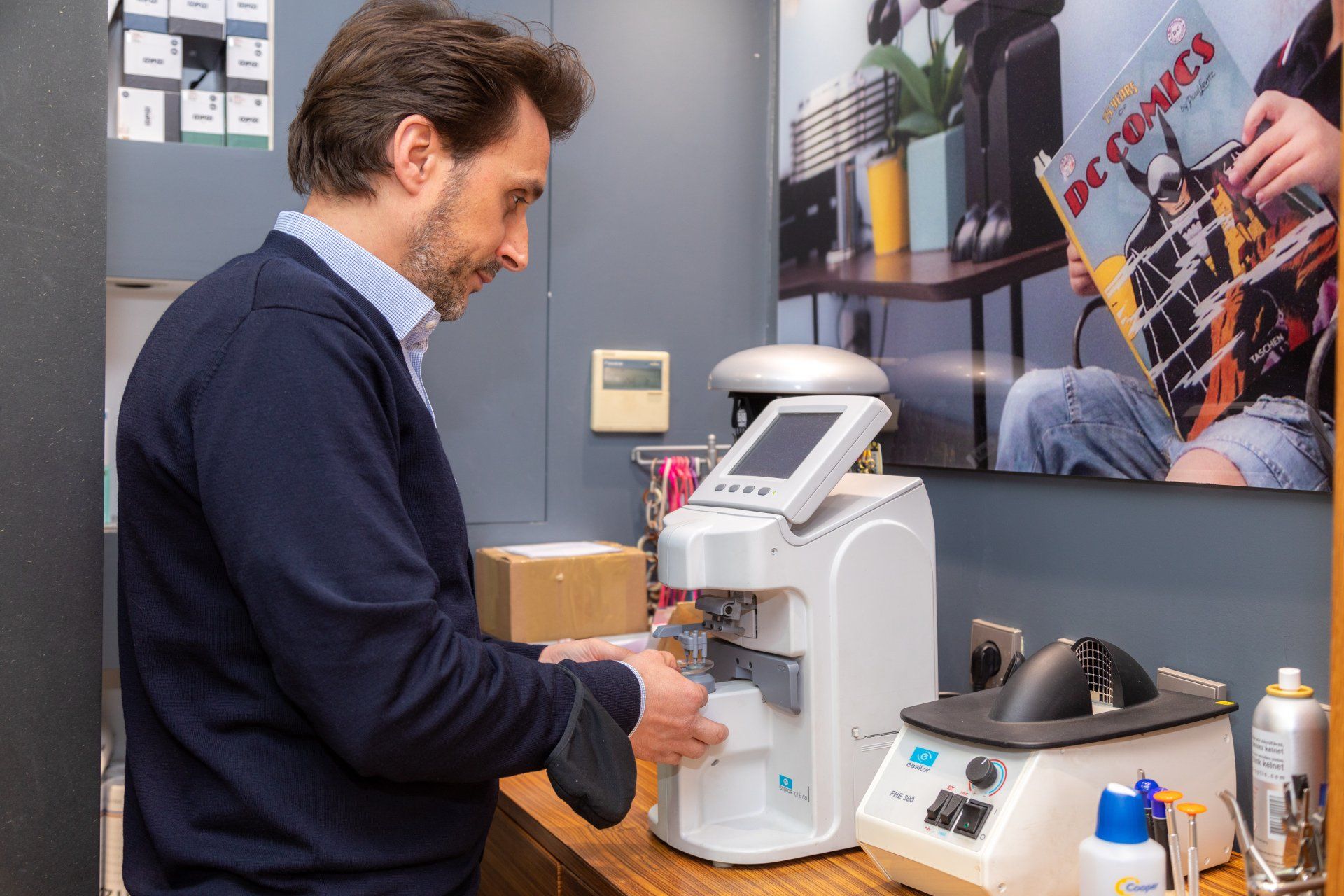 Un homme utilise du matériel d'optique dans un magasin. Il tient une monture et travaille sur une machine à écran.