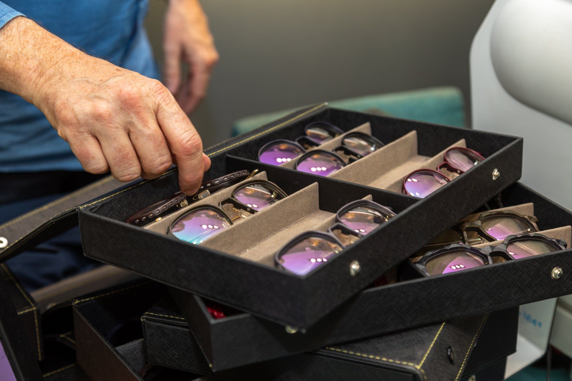 Une main tend la main vers des lunettes de soleil dans une vitrine noire à plusieurs niveaux, à l'intérieur. On aperçoit les verres teintés violets.