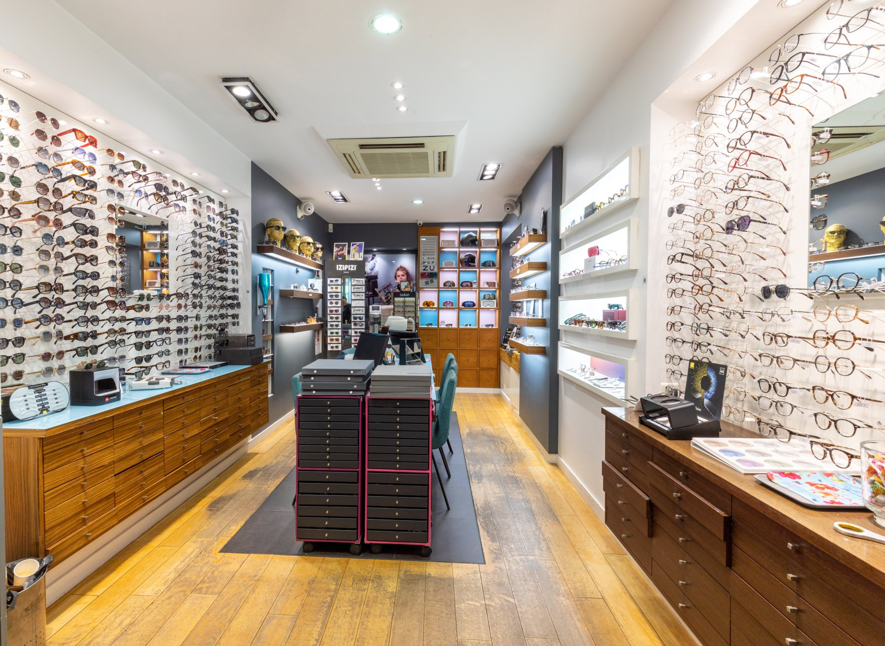 Intérieur d'un magasin d'optique avec présentoirs à lunettes, parquet et éclairage encastré.
