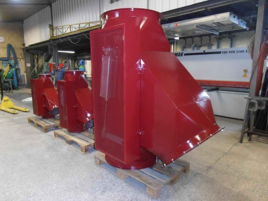 Quatre pièces de conduits métalliques rouges sur des palettes dans un environnement d'usine.