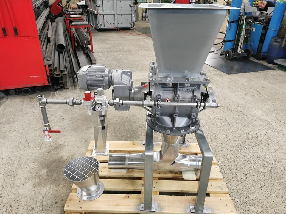 Machine industrielle de traitement de poudre sur palette, avec des composants argentés et gris, dans un environnement d'atelier.