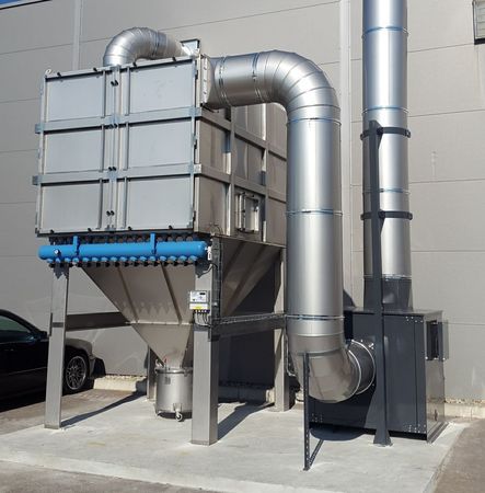 Grand dépoussiéreur industriel avec conduits, extérieur. Métal gris, tuyaux bleus, à côté d'un bâtiment.