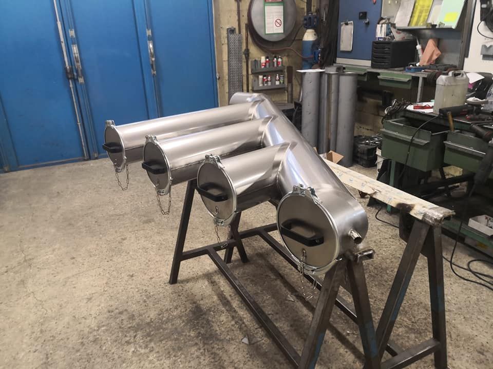 Collecteur en métal argenté à quatre ouvertures, sur un support en métal, dans un atelier.