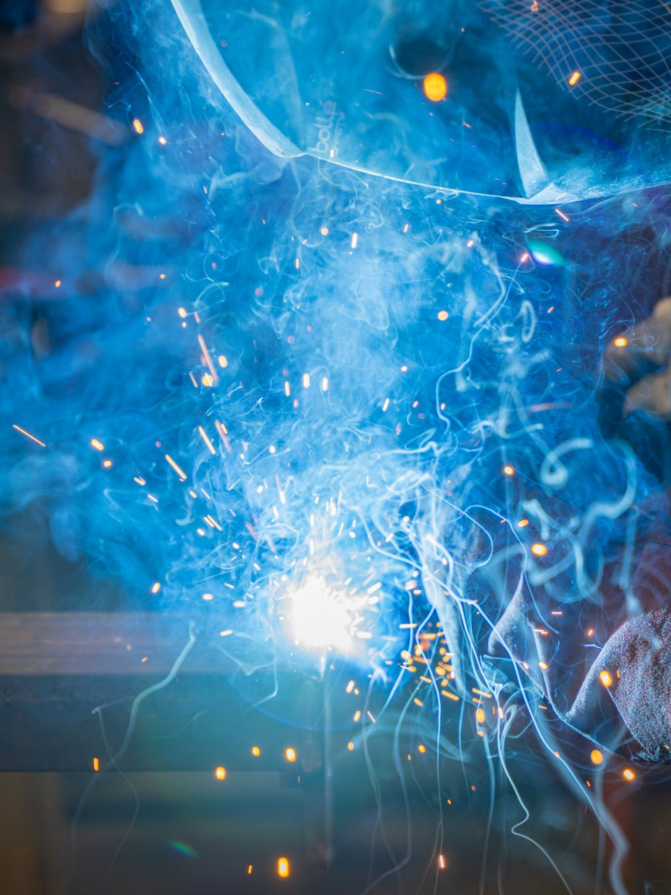 Des étincelles de soudage dans une lumière bleu vif, de la fumée et des particules métalliques.