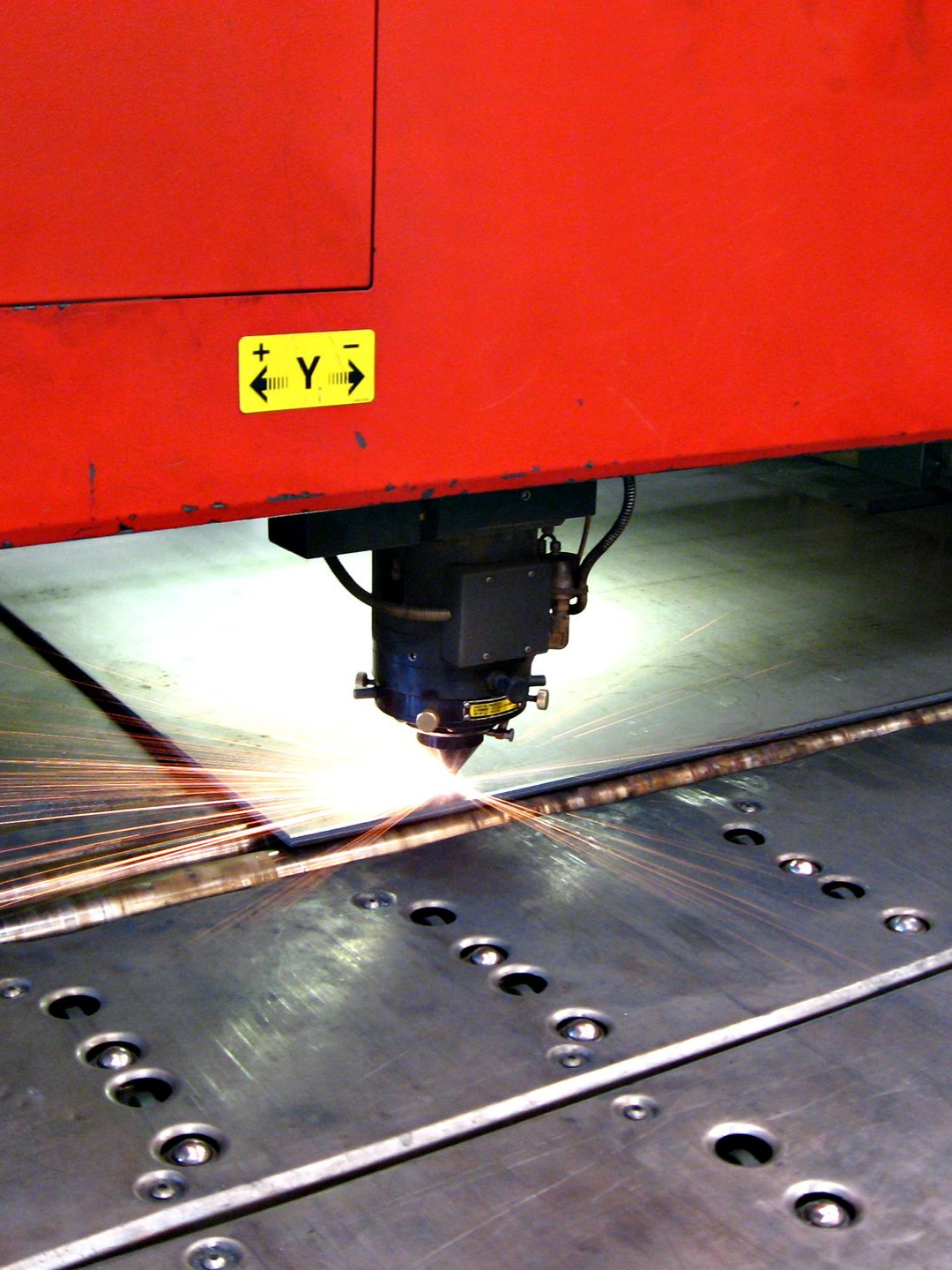 Découpe laser rouge d'une tôle, étincelles volantes.