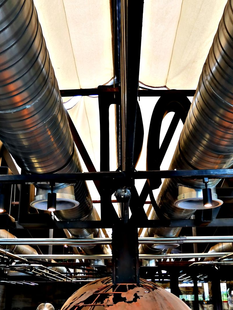 Plafond industriel avec conduits métalliques, poutres de soutien et éclairage apparent.