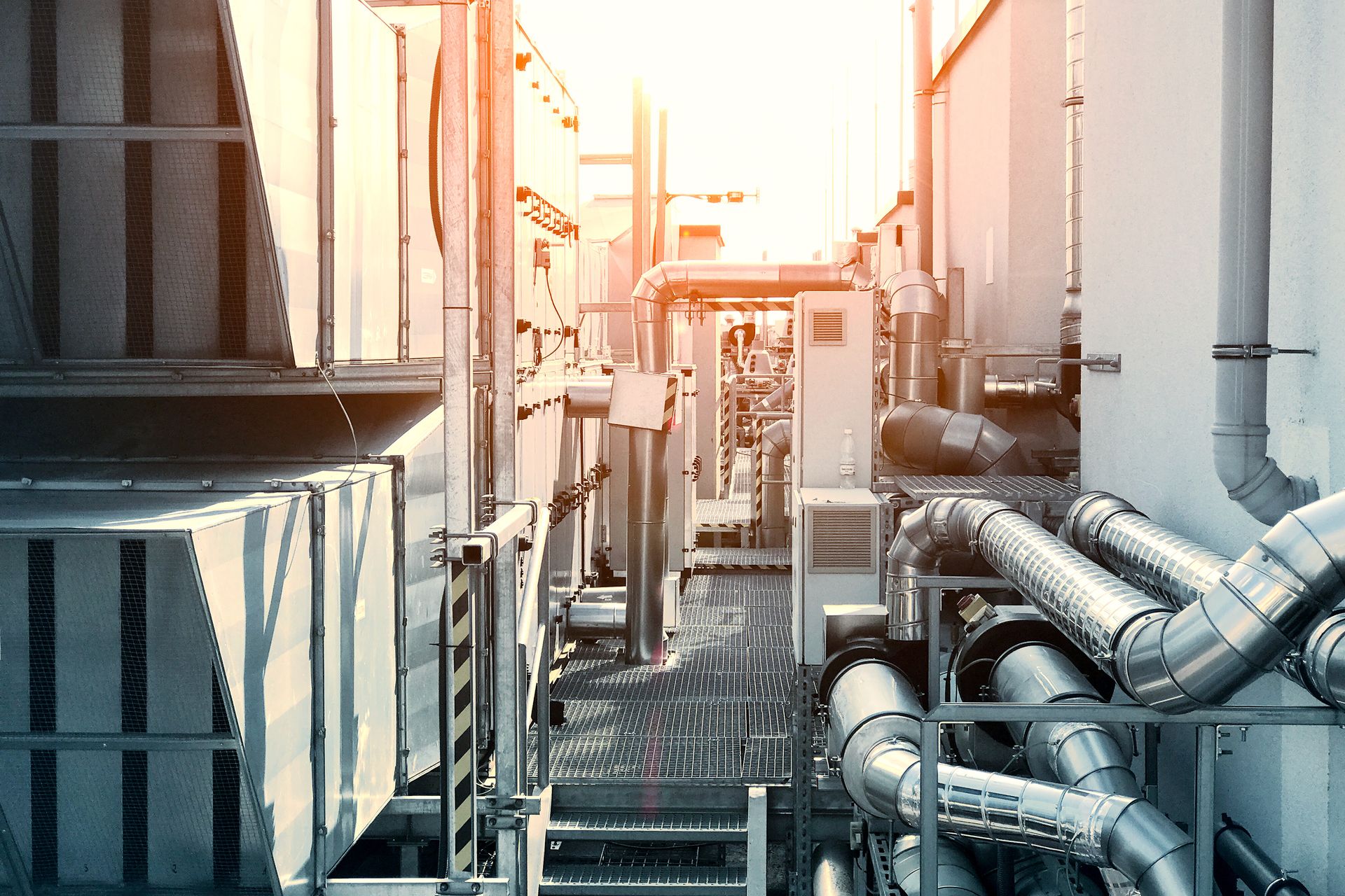 Toit industriel avec tuyaux métalliques, machines et soleil éclatant.