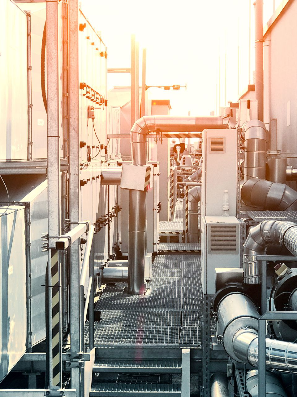 Équipement industriel sur le toit ; tuyaux, évents et machines ; soleil éclatant.
