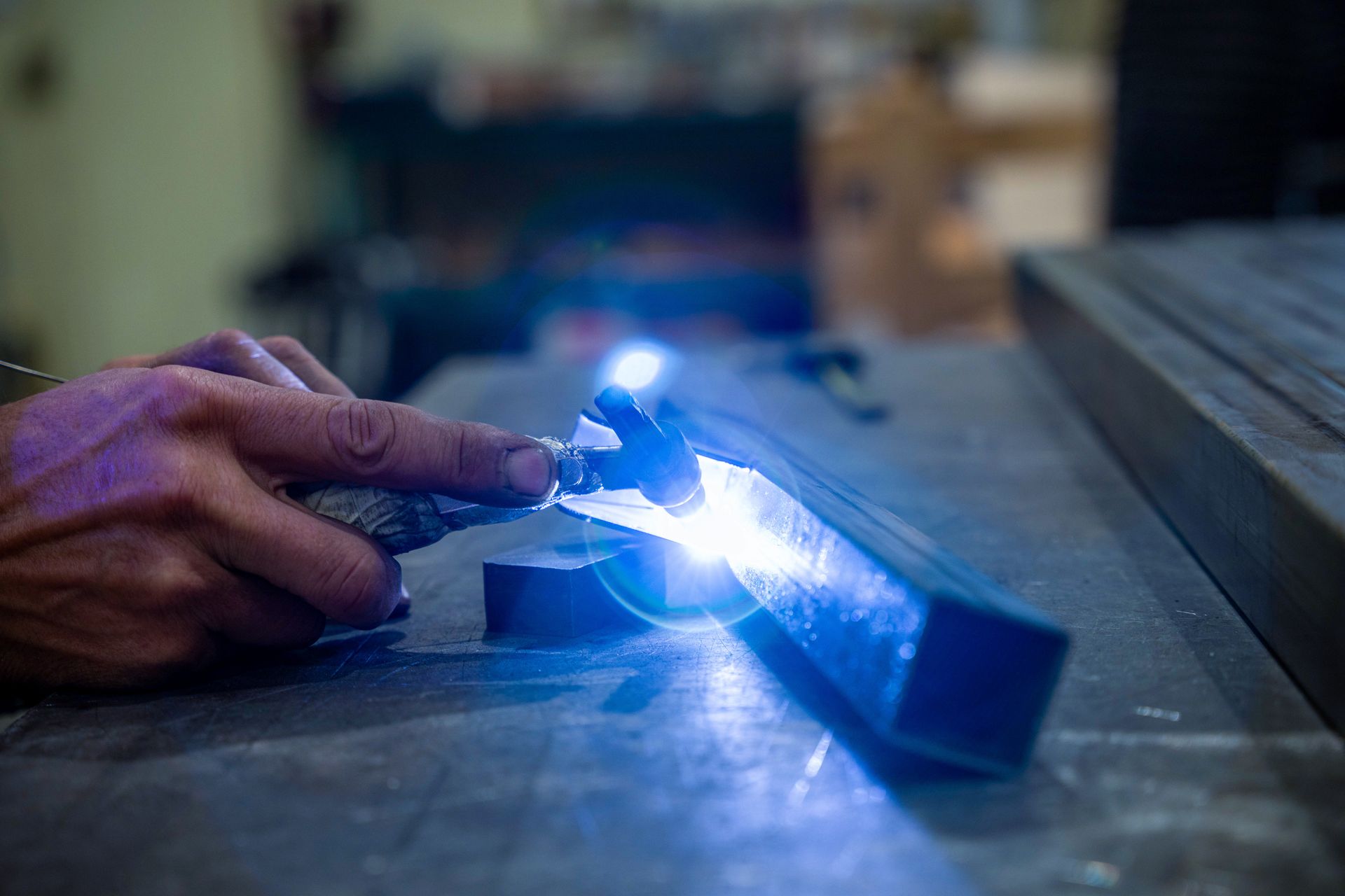 Une personne soude du métal avec une lumière bleue brillante dans un atelier.