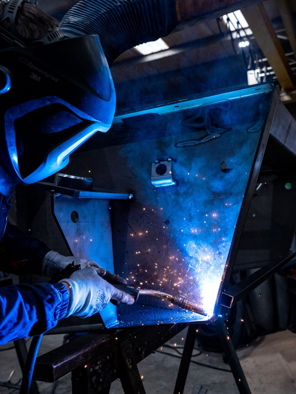 Soudeur en tenue de protection bleue soudant du métal, étincelles volantes.