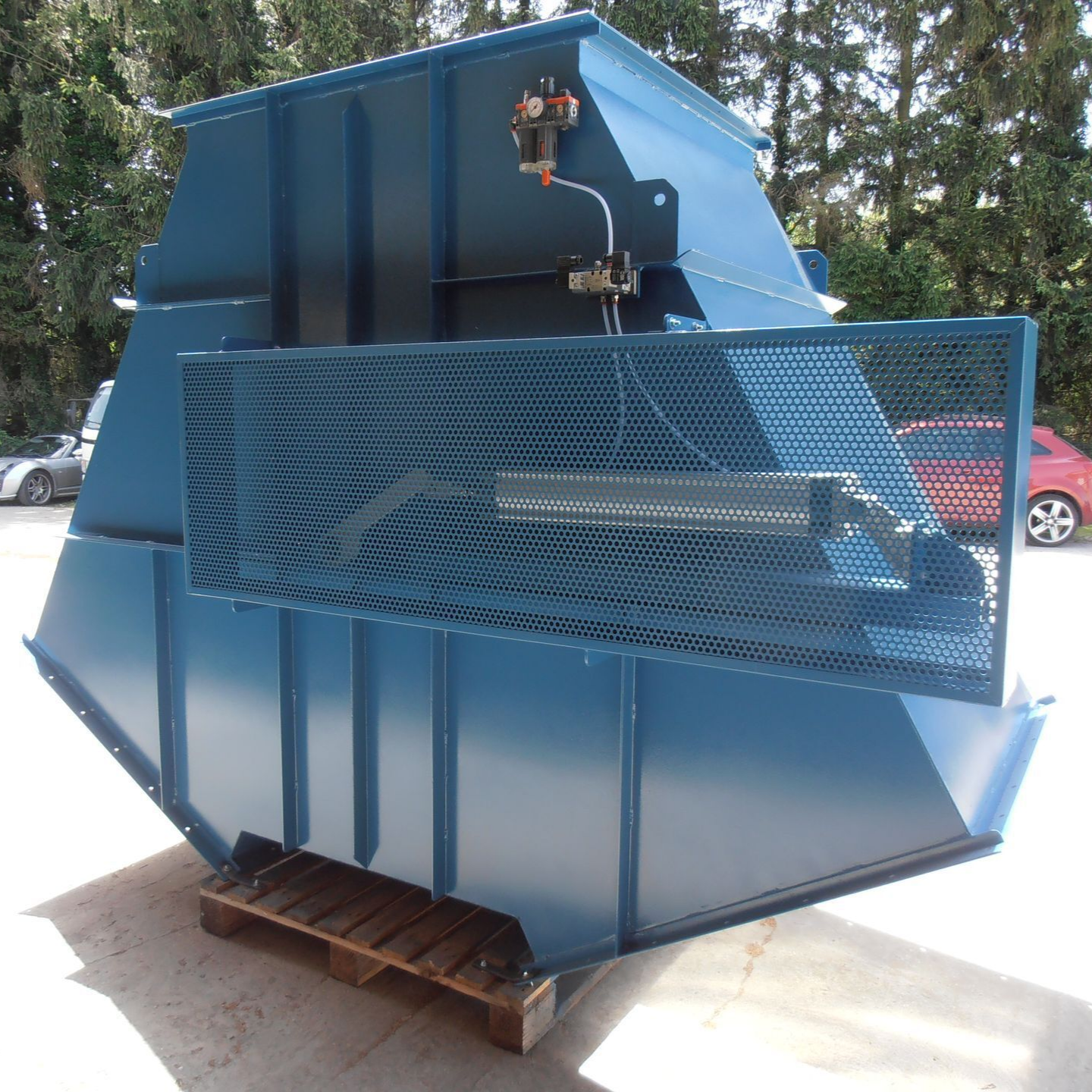 Compacteur de déchets industriels bleu avec grille de protection métallique, pour extérieur.