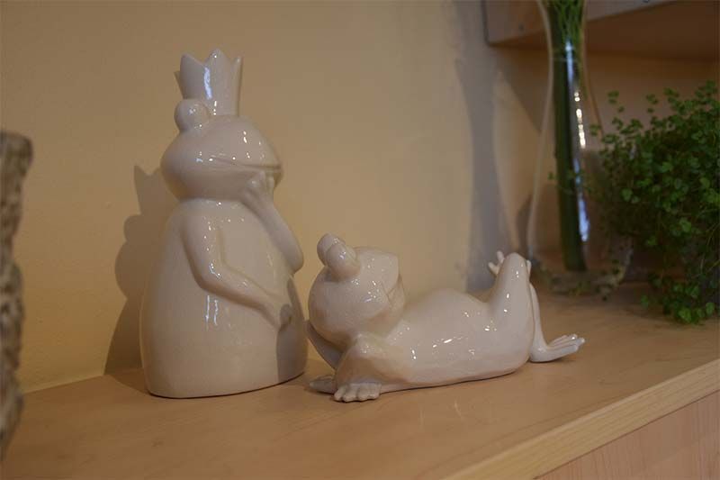 Zwei weiße Froschfiguren sitzen auf einem Holzregal.