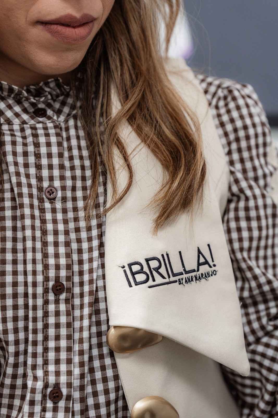 Mujer que lleva una camisa a cuadros marrón y blanca con una bufanda blanca que dice 