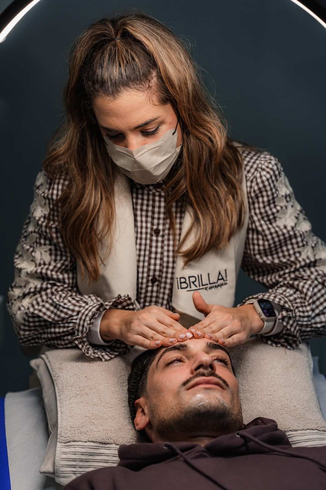 Una persona dando un masaje facial a una persona acostada en una cama; entorno interior.