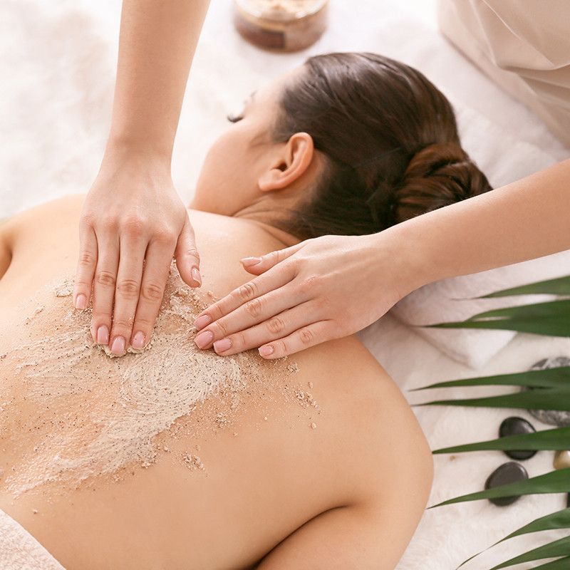 Terapeuta de spa aplicando un exfoliante con masaje en la espalda de un cliente durante un tratamiento corporal