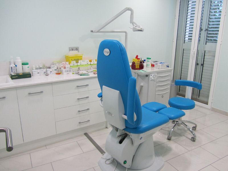Sillón dental azul en una luminosa sala de consulta con armarios blancos y lavabo.