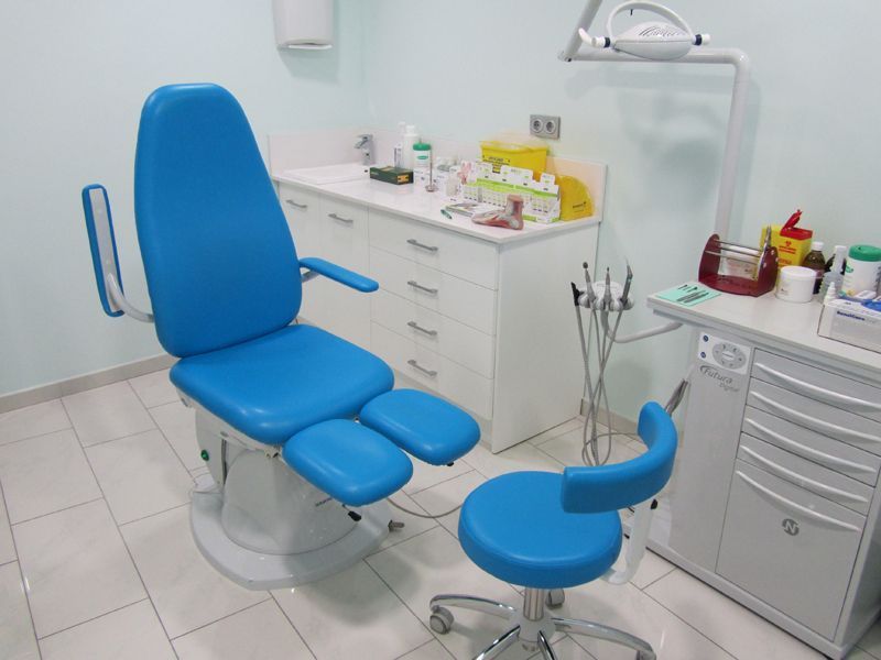 Sillón dental azul en una sala de examen dental limpia con instrumental y armarios.