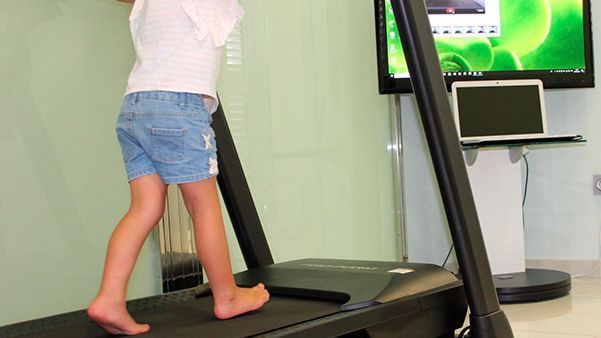 Un niño camina sobre una cinta de correr en una sala de consulta, con un monitor y el equipo cerca.