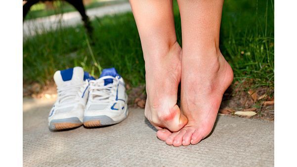 Pies descalzos junto a zapatillas blancas en una acera cerca del césped.