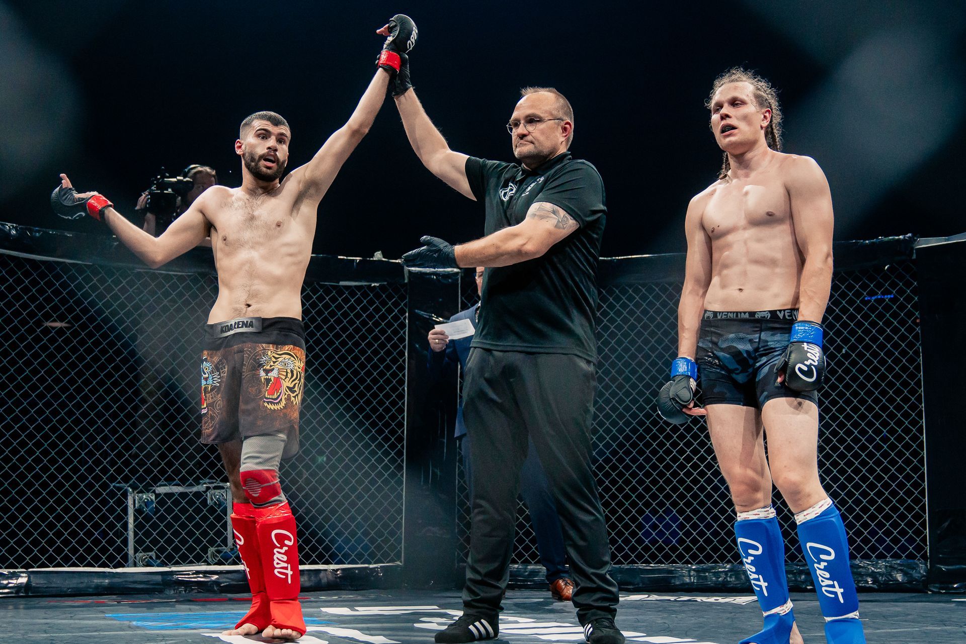 MMA-tuomari nostaa voittajan käden hävinneen ottelijan vieressä kehässä