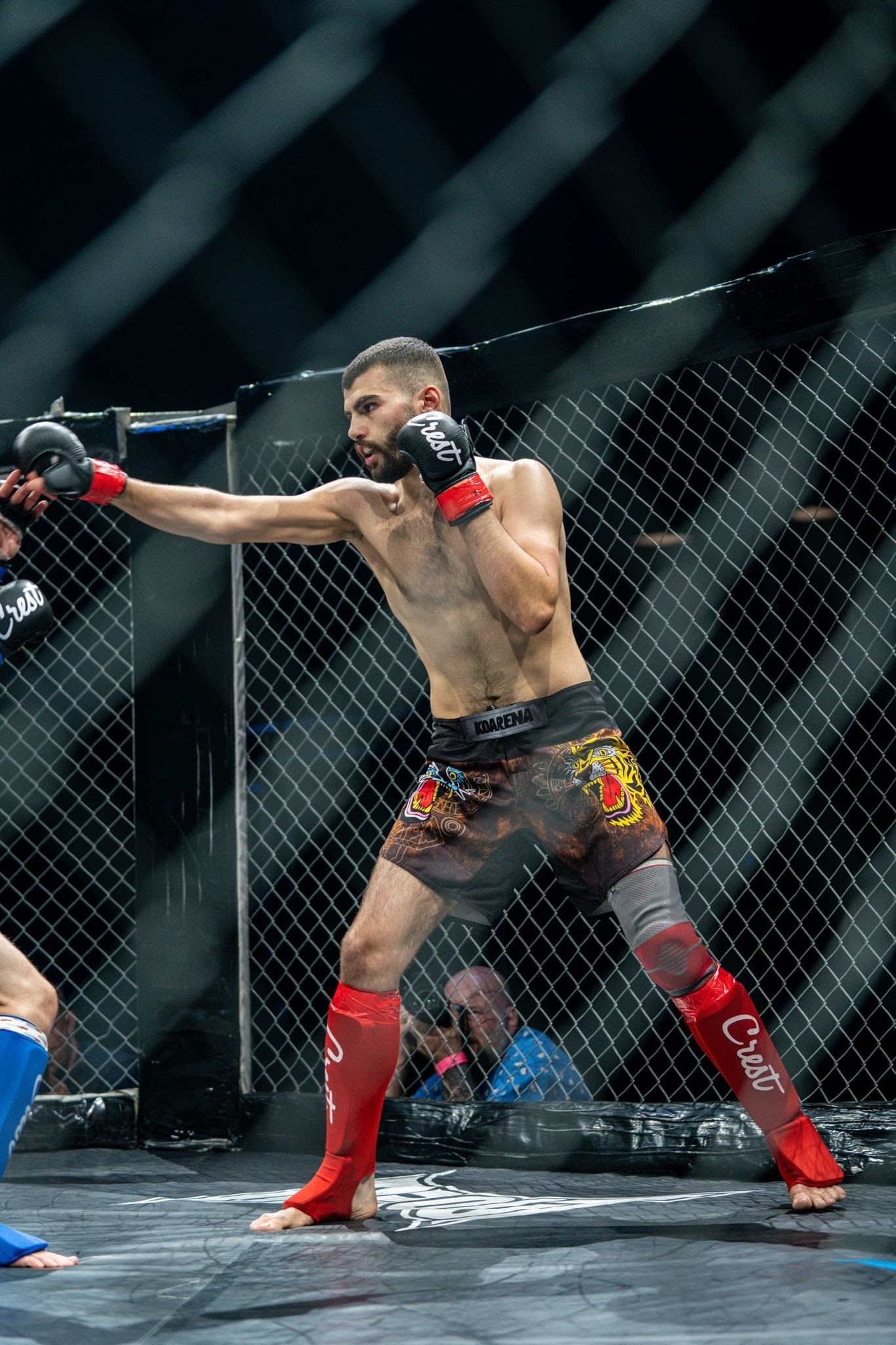 Muay Thai -ottelija mustissa hanskoissa ja punaisissa säärisuojissa lyö häkkikehässä