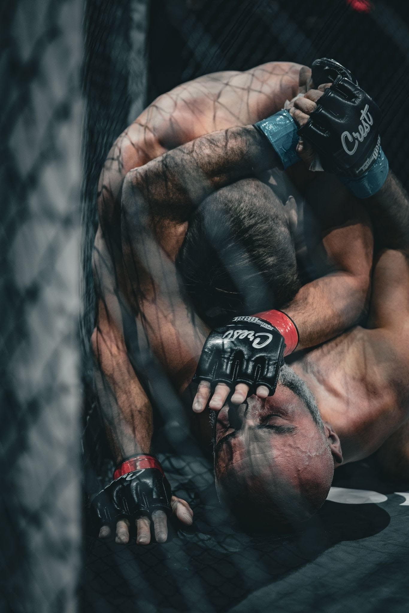 MMA-ottelija kyykistyy puolustusasennossa mustissa hanskoissa ja punaisissa rannetuissa verkkoaidan takana