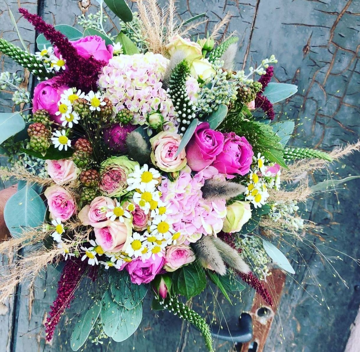 Rosa-weißer Blumenstrauß mit Rosen, Gänseblümchen und Grün vor rustikalem blauem Hintergrund