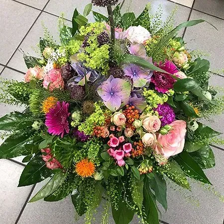 Farbenfroher gemischter Blumenstrauß aus rosa, lila, orangefarbenen und grünen Blumen mit üppigem Grün
