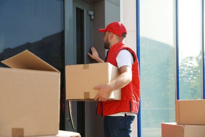 Un repartidor lleva una caja de cartón a un edificio.