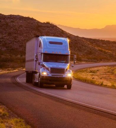 Un camión semirremolque circula por una carretera con curvas al atardecer.