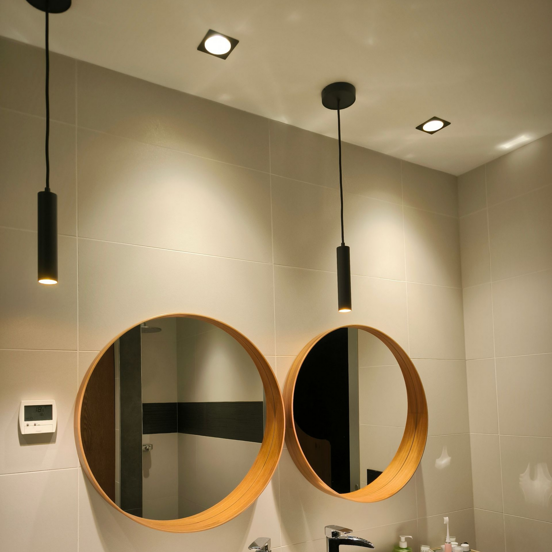 Salle de bains avec deux miroirs ronds, des suspensions lumineuses et des spots encastrés.