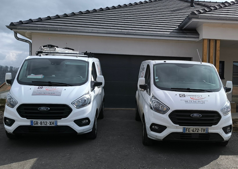 Deux fourgonnettes Ford Transit blanches garées devant une maison au toit gris foncé.