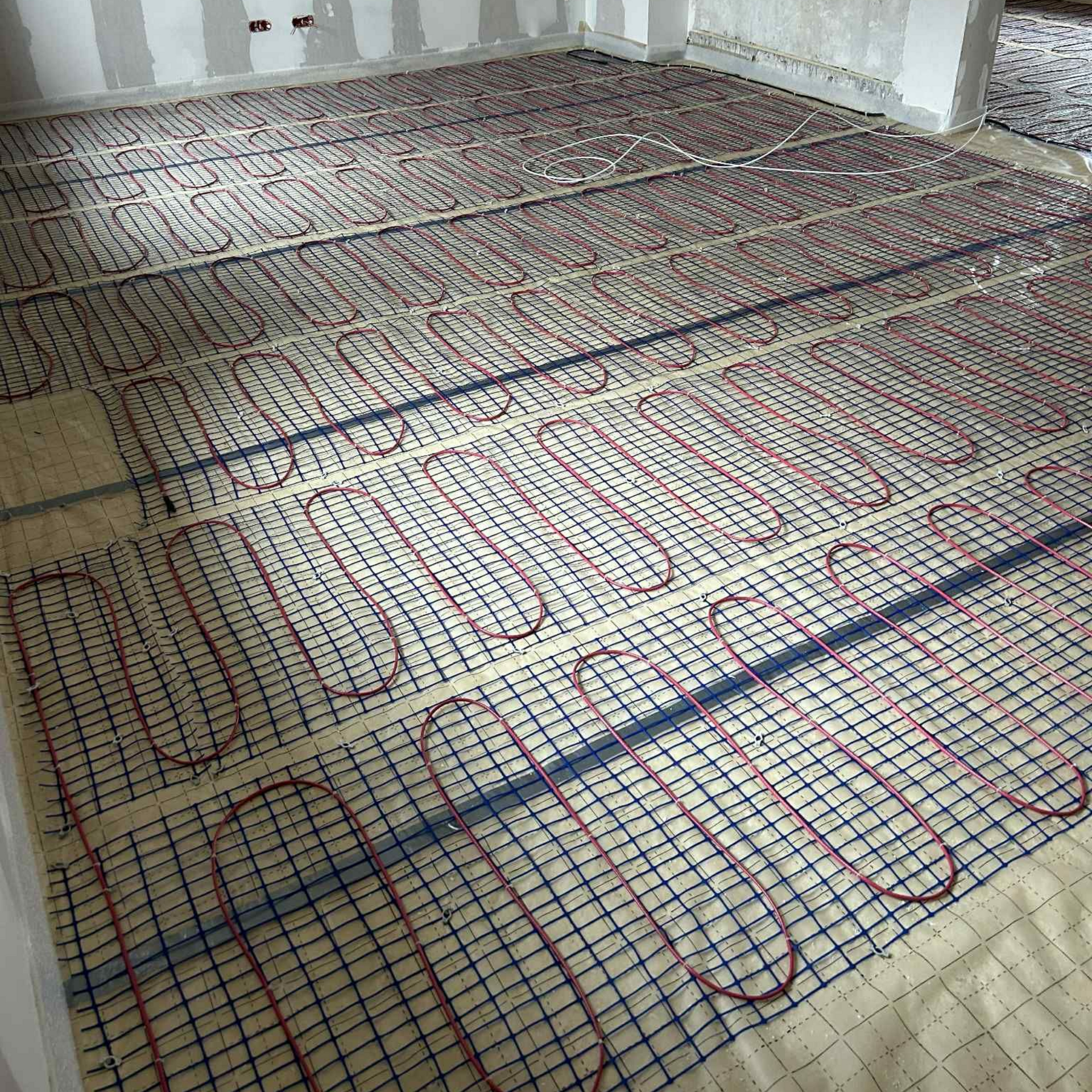 Installation d'un système de chauffage au sol : grille de tuyaux rouges, treillis bleu, intérieur de la pièce.