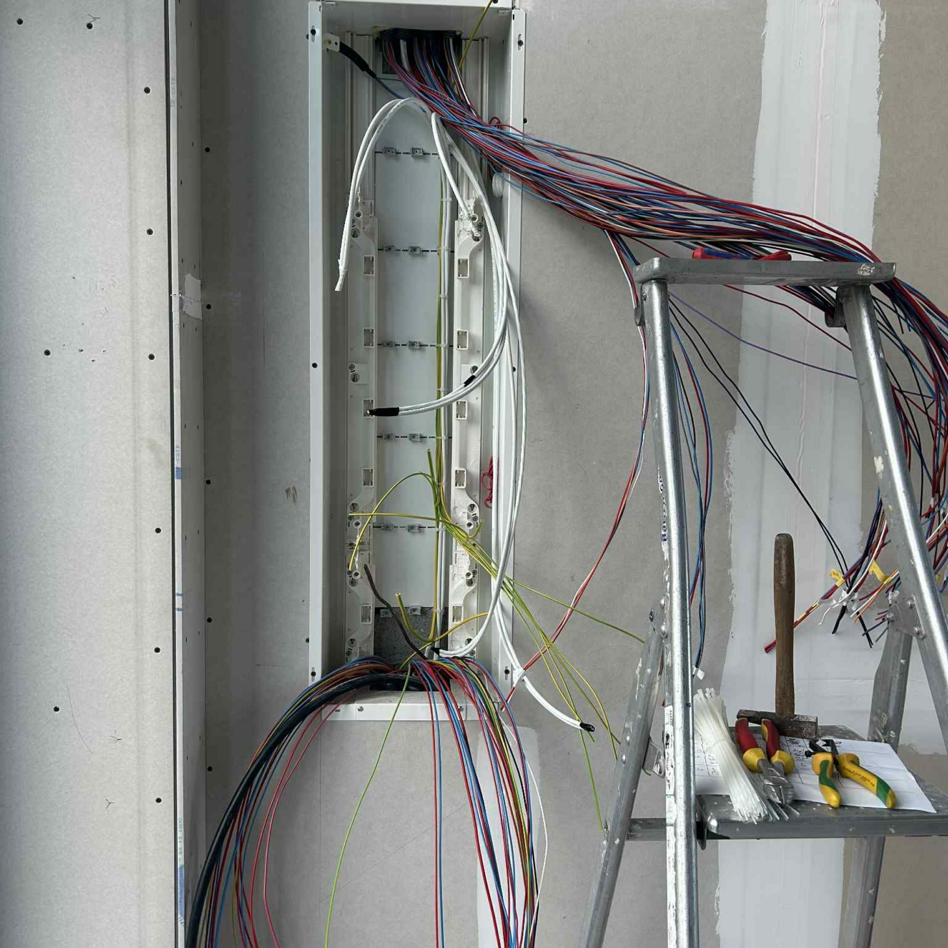 Câblage électrique dans une boîte murale ; les fils sont colorés. Un cadre de support métallique se trouve à proximité.