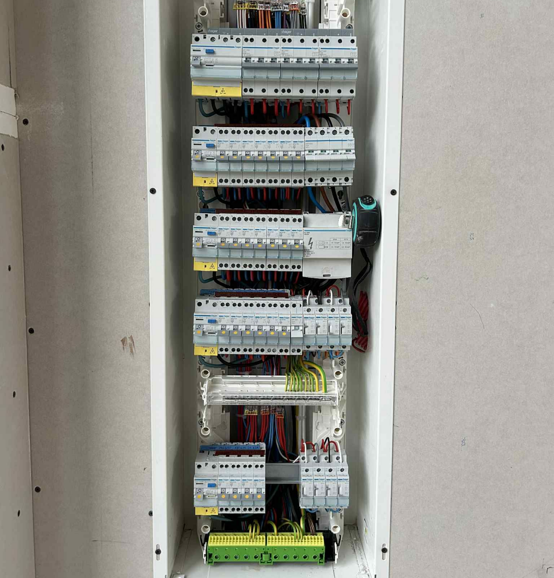 Tableau électrique avec de nombreux disjoncteurs, câbles et blocs de mise à la terre, monté dans un mur.