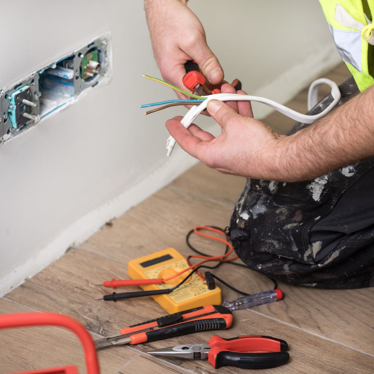 Un électricien effectue des travaux de câblage sur une prise électrique.