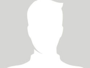 Ein Mechaniker lächelt in einer Werkstatt, er trägt ein graues Hemd, die Arme hängen seitlich herab.